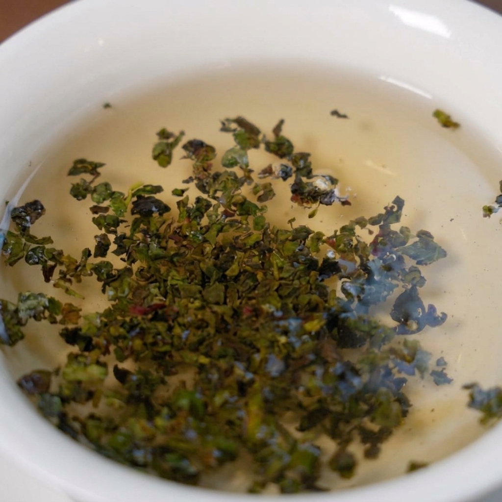 Feuilles de thé vert Tieguanyin qui se déploient et infusent dans un bol blanc rempli deau chaude.