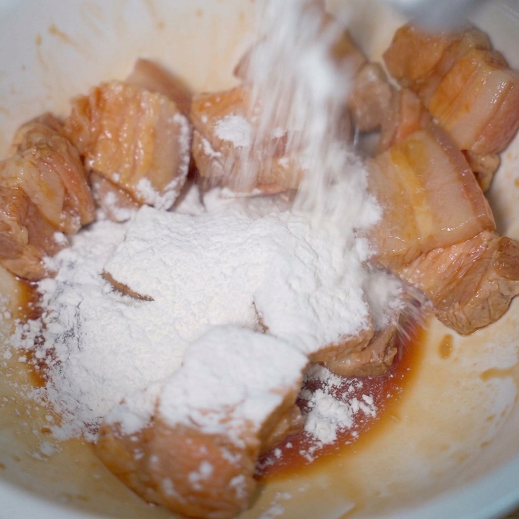 Tranches de porc pâles dans un bol, saupoudrées dune épaisse couche de fécule de tapioca blanche.