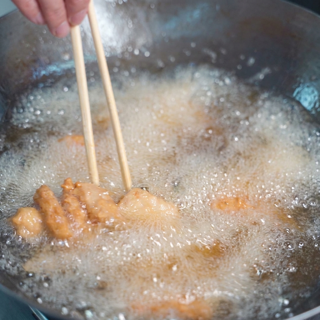 Morceaux de porc enrobés en train de frire dans de lhuile dorée bouillonnante, remués avec des baguettes en bois.