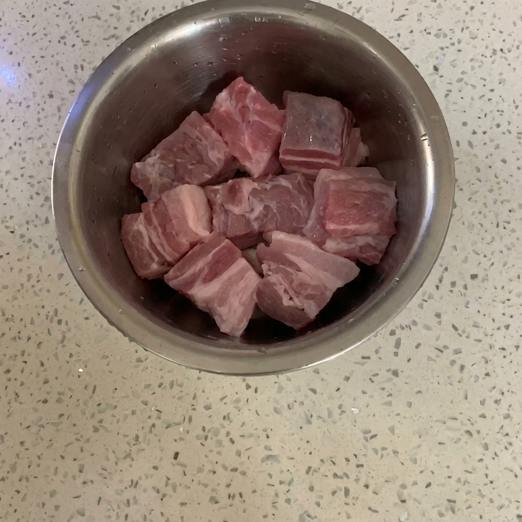 Cubes de poitrine de porc crus dans un bol mélangeur en acier inoxydable sur un plan de travail.