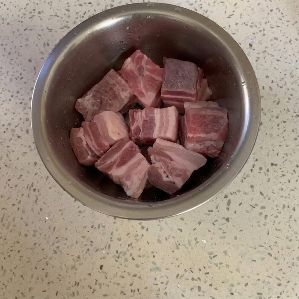 Cubes de porc dans un bol métallique légèrement enrobés de sucre cristallisé.