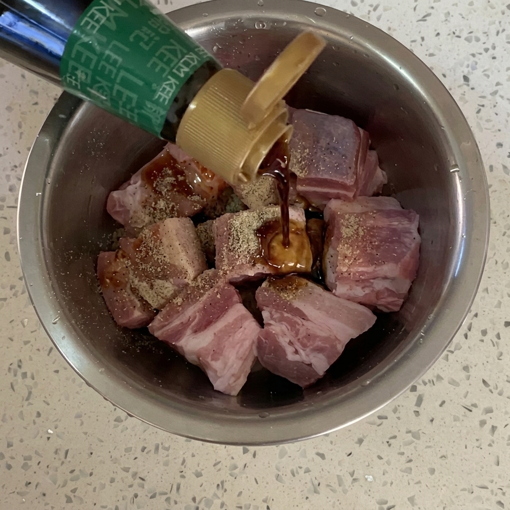 Sauce soja versée depuis une bouteille sur les cubes de porc assaisonnés.
