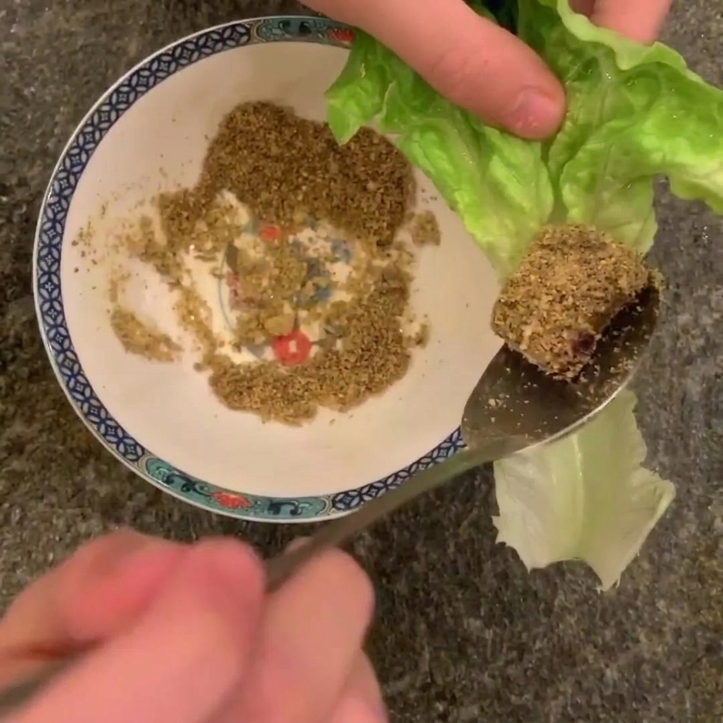 Gros plan dune cuillère tenant un morceau de porc cuit enrobé de cacahuètes au-dessus dune feuille de laitue romaine.