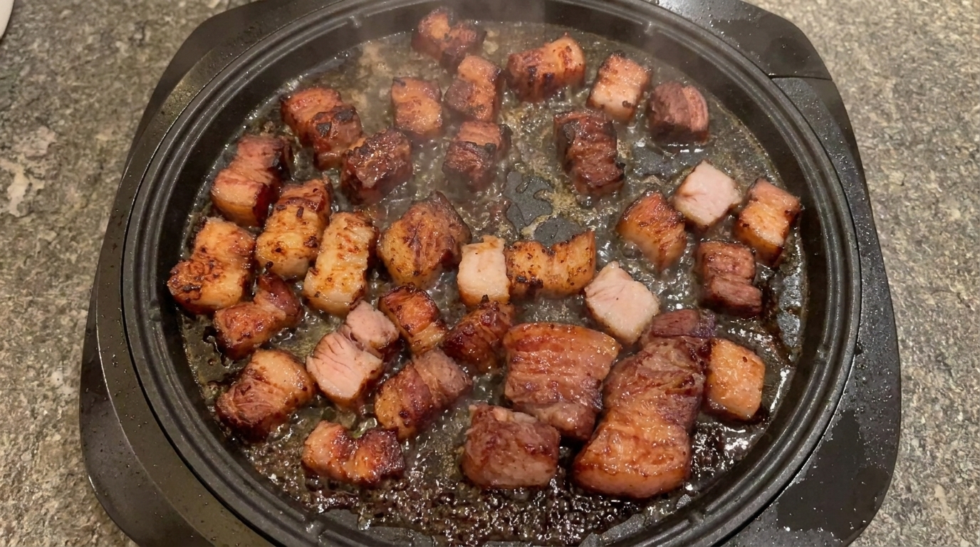 Morceaux de poitrine de porc caramélisés et dorés grésillant dans une poêle.