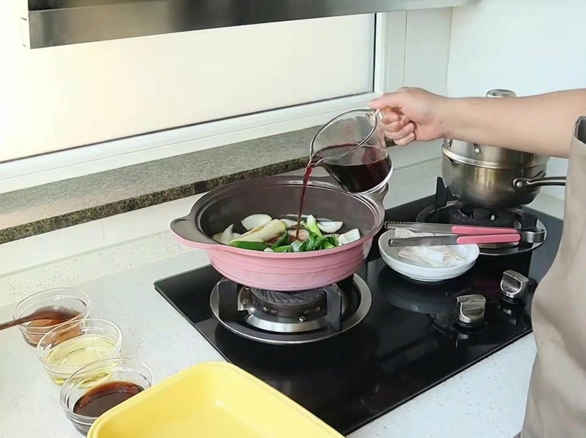 Main versant du vin rouge depuis un verre mesureur dans une poêle contenant les oignons et aromates.