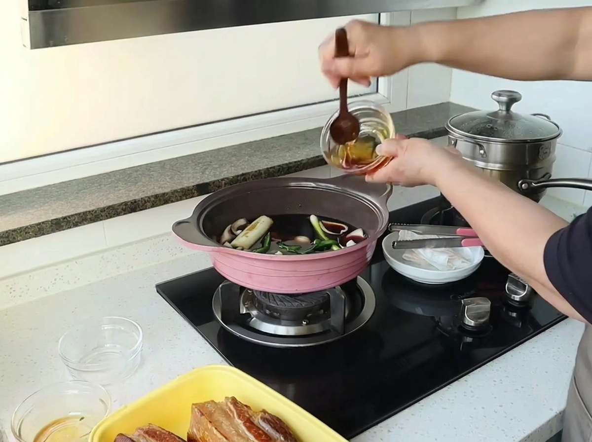Main versant du miel depuis un petit bol en verre dans une cocotte rose remplie dun mélange liquide sombre.