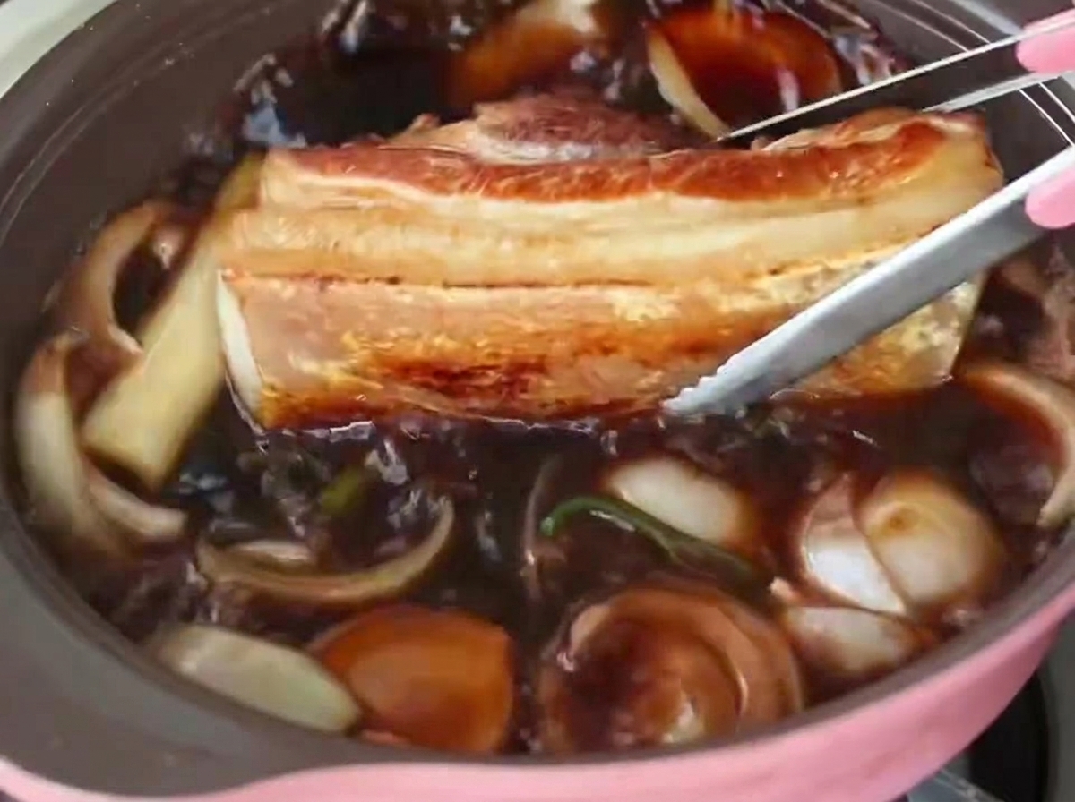 Pinces plaçant une épaisse tranche de poitrine de porc dans un bouillon sombre et bouillonnant.
