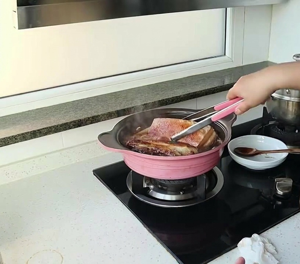 Personne utilisant une pince pour retourner de gros morceaux de porc mijotant dans une sauce sombre.