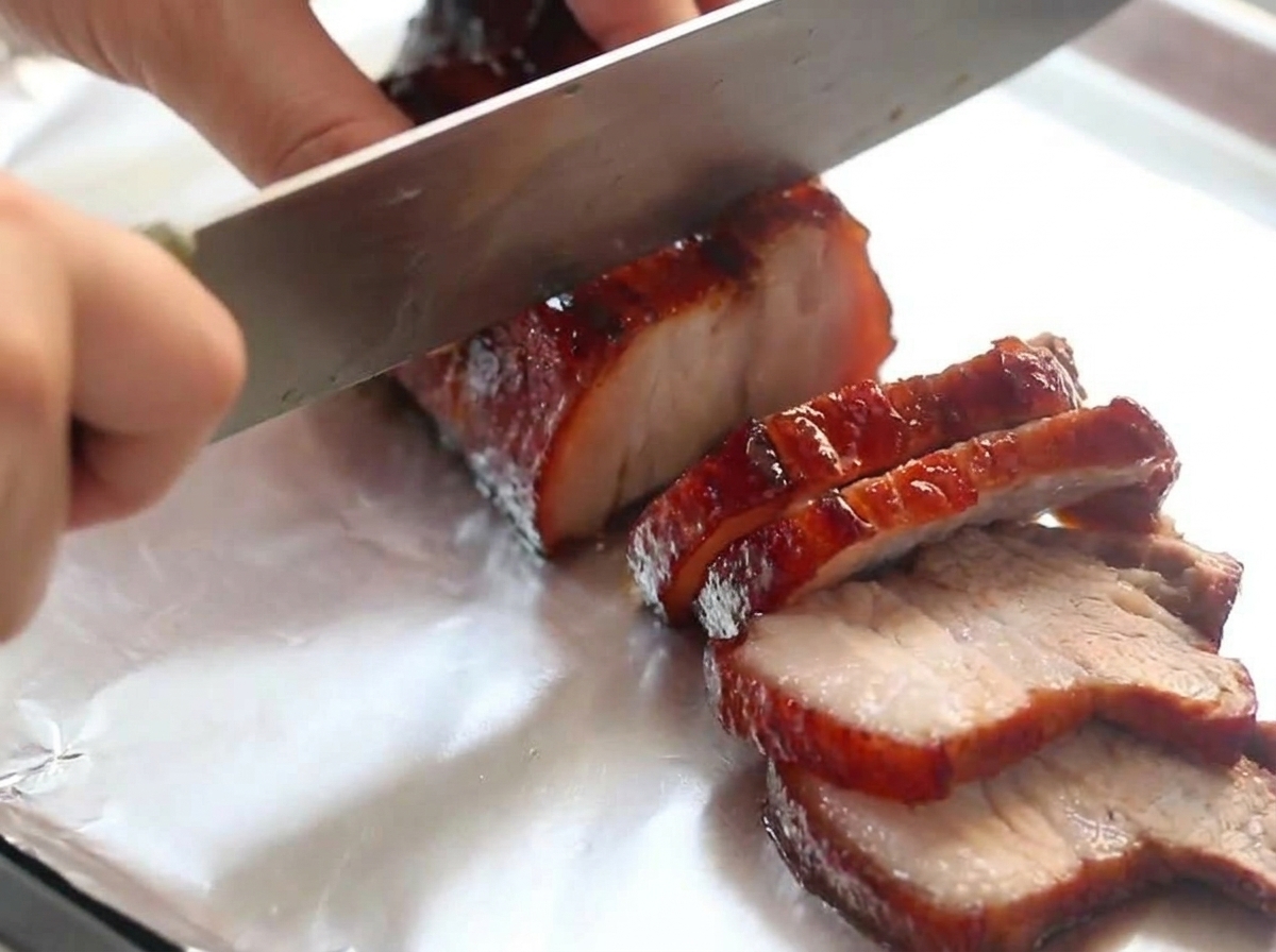 Couteau de chef tranchant une pièce de porc laqué au vin rouge sur du papier aluminium.