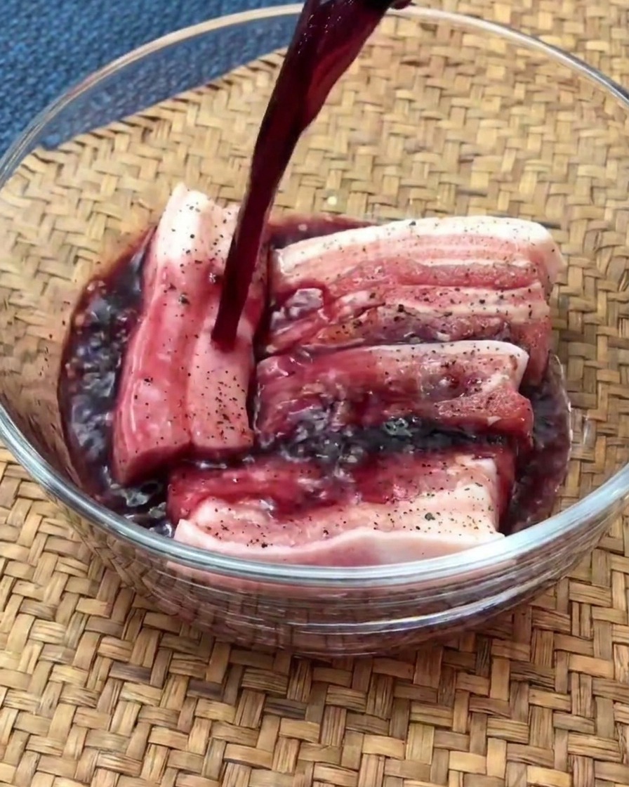 Tranches de poitrine de porc crue marinant dans un bol en verre rempli de vin rouge.