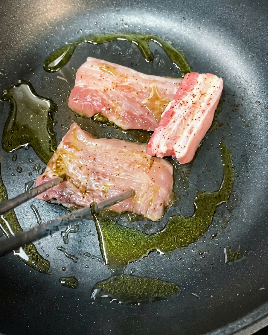 Tranches de poitrine de porc marinée dorer dans une poêle chaude avec de lhuile dolive.