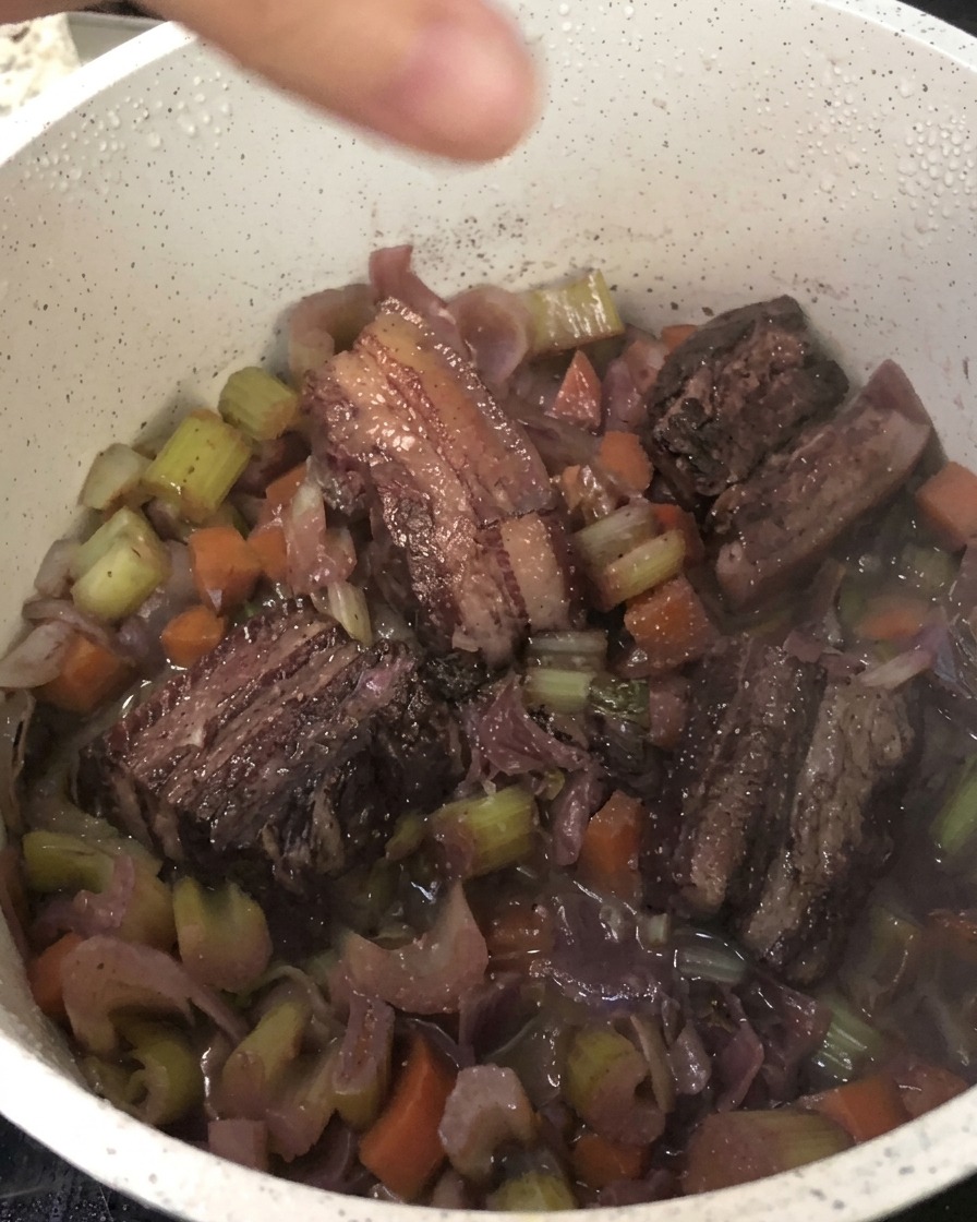 Moulin à poivre noir frais au-dessus de la cocotte contenant le porc braisé et les légumes.