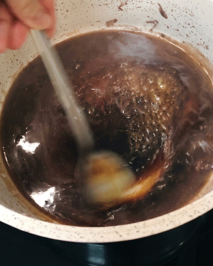 La réduction de vin rouge frémit et sépaissit dans la cocotte tout en étant remuée.