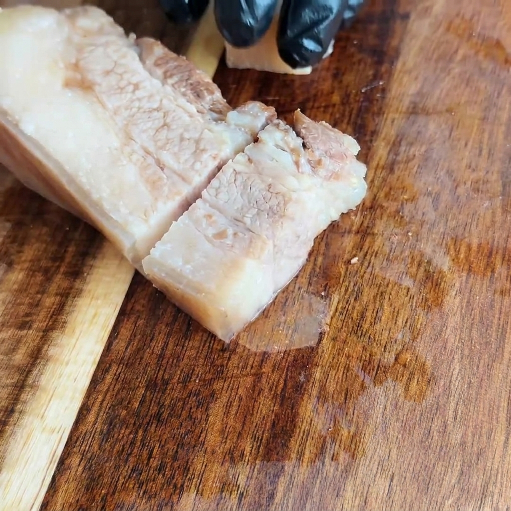 Poitrine de porc refroidie coupée en carrés réguliers sur une planche à découper en bois.