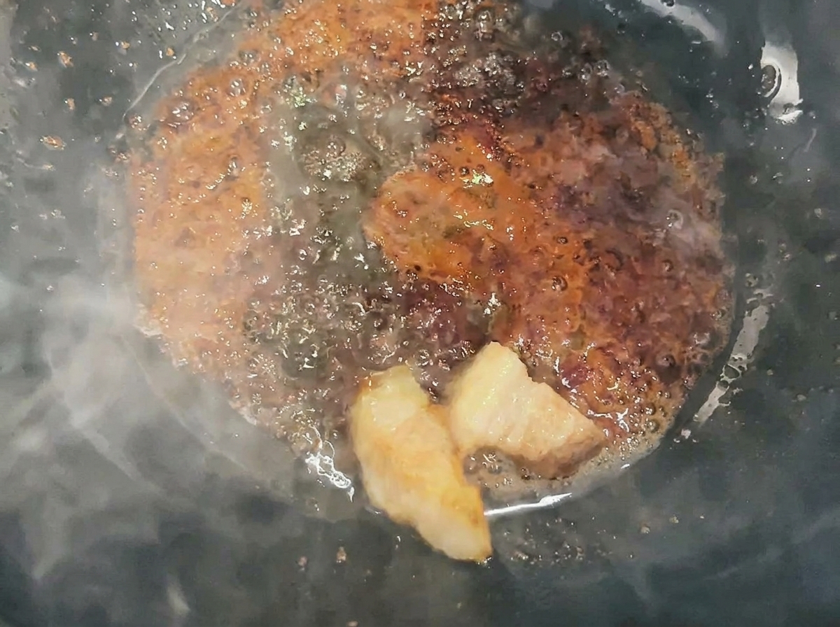 Cubes de porc mélangés et enrobés de caramel liquide dans un wok.