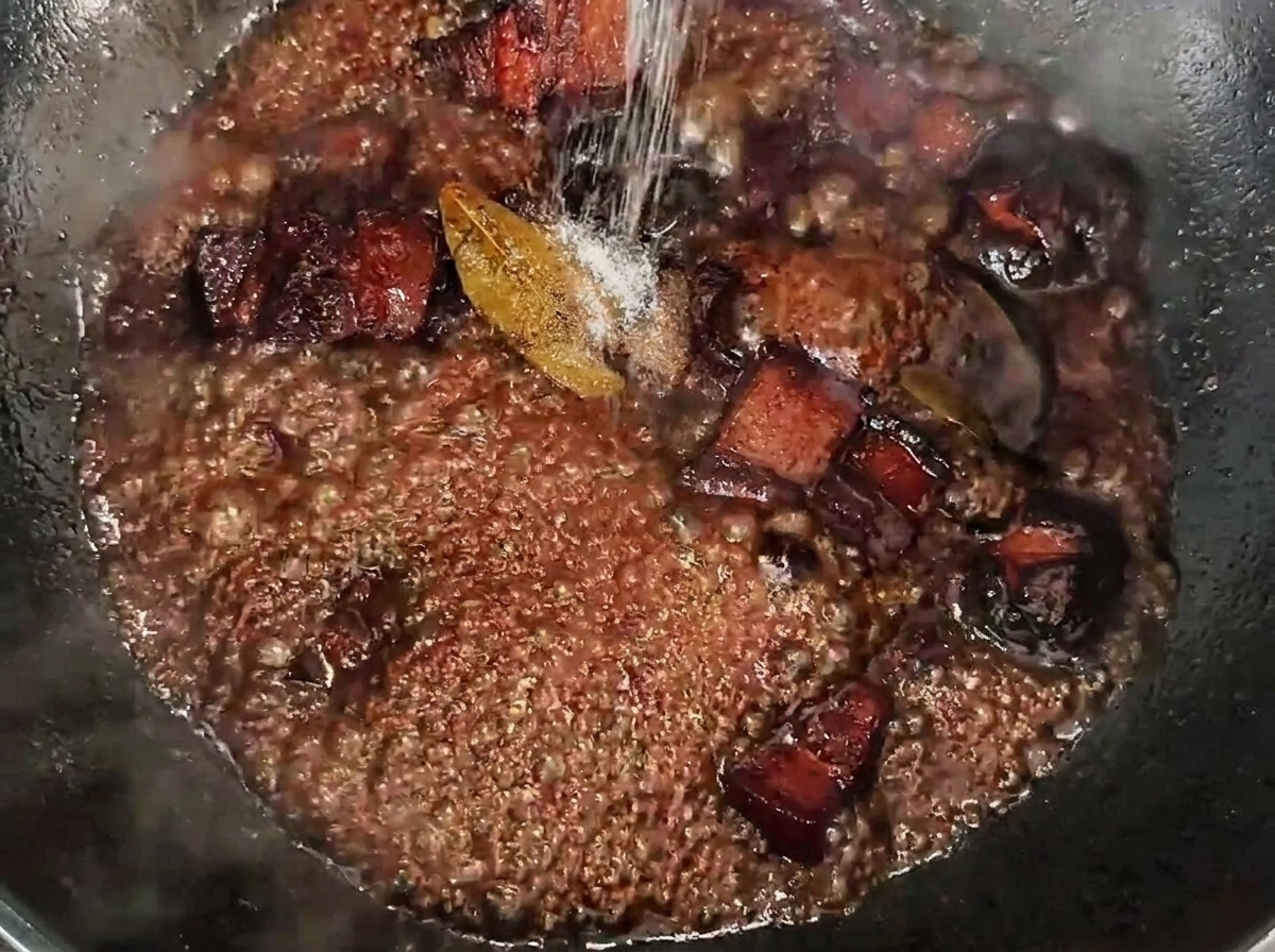 Sel saupoudré sur les cubes de porc mijotant dans une sauce riche et sombre.