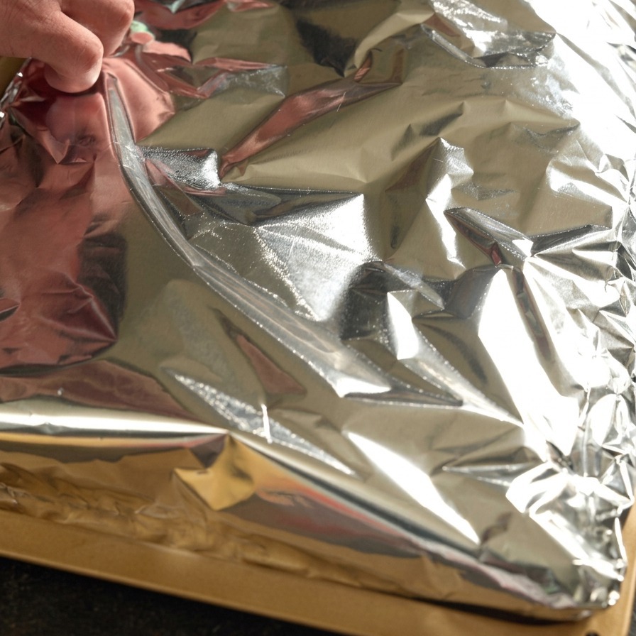 Des mains repliant hermétiquement du papier aluminium sur un rack de travers de porc assaisonné.