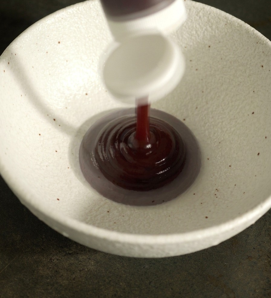 De la sauce barbecue rouge foncé et dautres condiments versés dans un bol en céramique blanche.