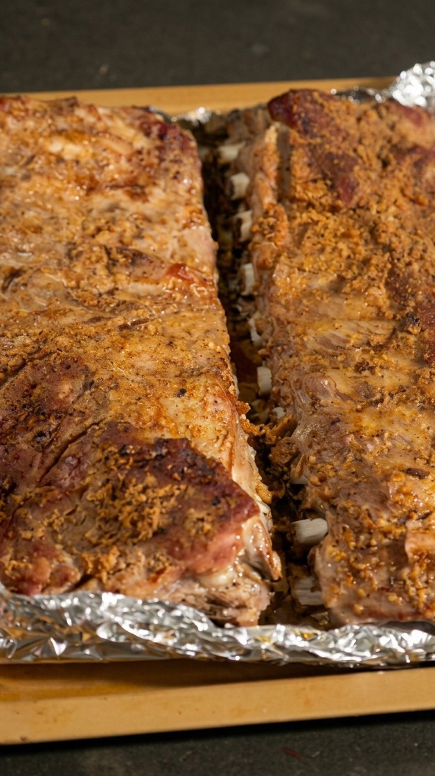 Deux racks de travers de porc cuits sur une plaque, le papier aluminium ouvert laissant apparaître la viande.