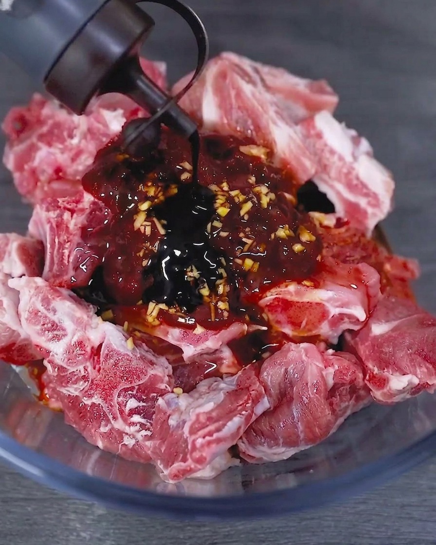Sauce soja foncée versée depuis une bouteille dans un bol contenant les travers de porc crus marinés.