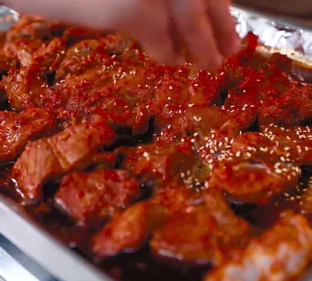 Gros plan sur les travers de porc rôtis dans leur plateau, avec des graines de sésame blanc saupoudrées sur la surface brillante recouverte de sauce rouge.