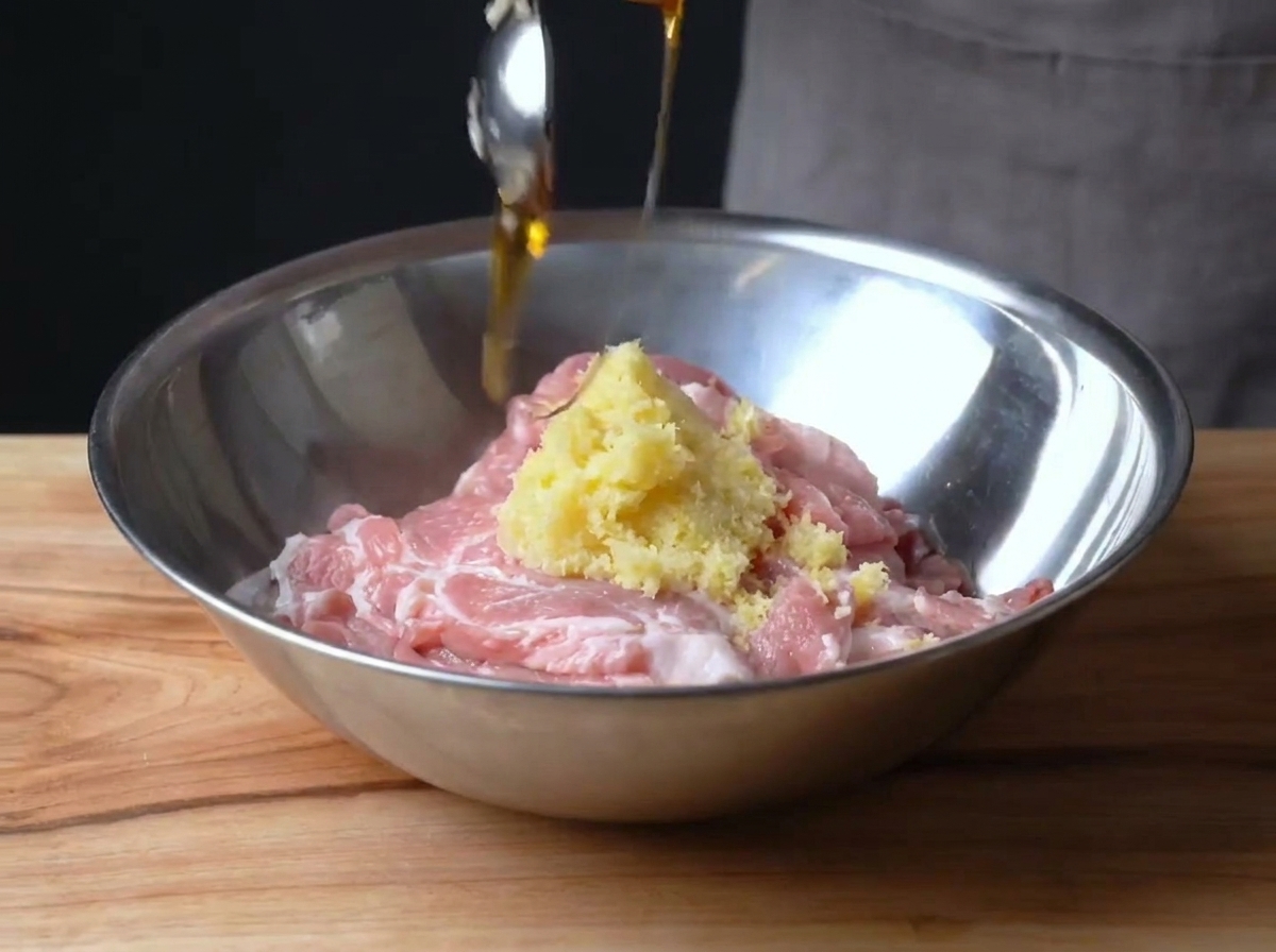 Tranches de porc dans un bol en métal mélangées avec du zeste de citron et du sirop de maïs.