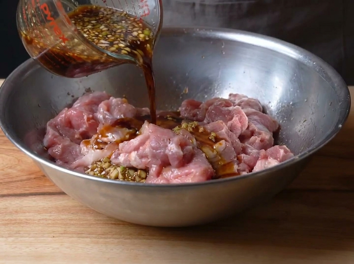 La marinade versée sur le porc dans le bol en métal.