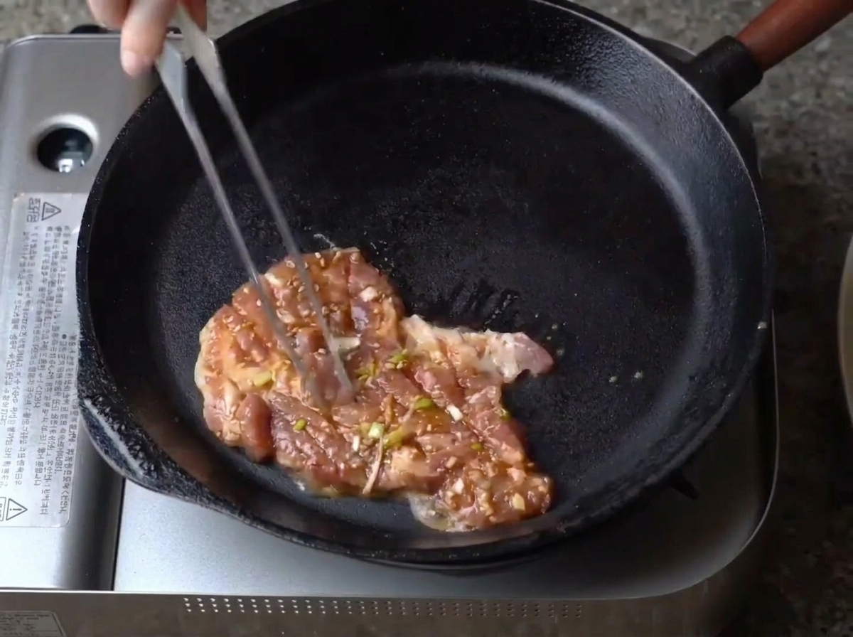 Une tranche de porc mariné placée dans une poêle en fonte chaude.