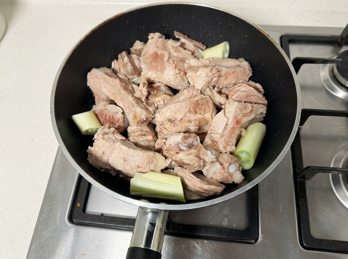 Travers de porc crus et morceaux de ciboule reposant dans une poêle noire.