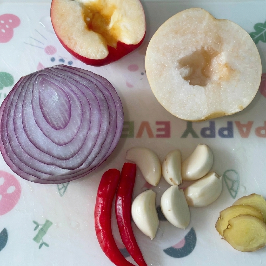 Moitié de pomme, doignon rouge et de poire avec des gousses dail, des piments et des tranches de gingembre sur une planche à découper.