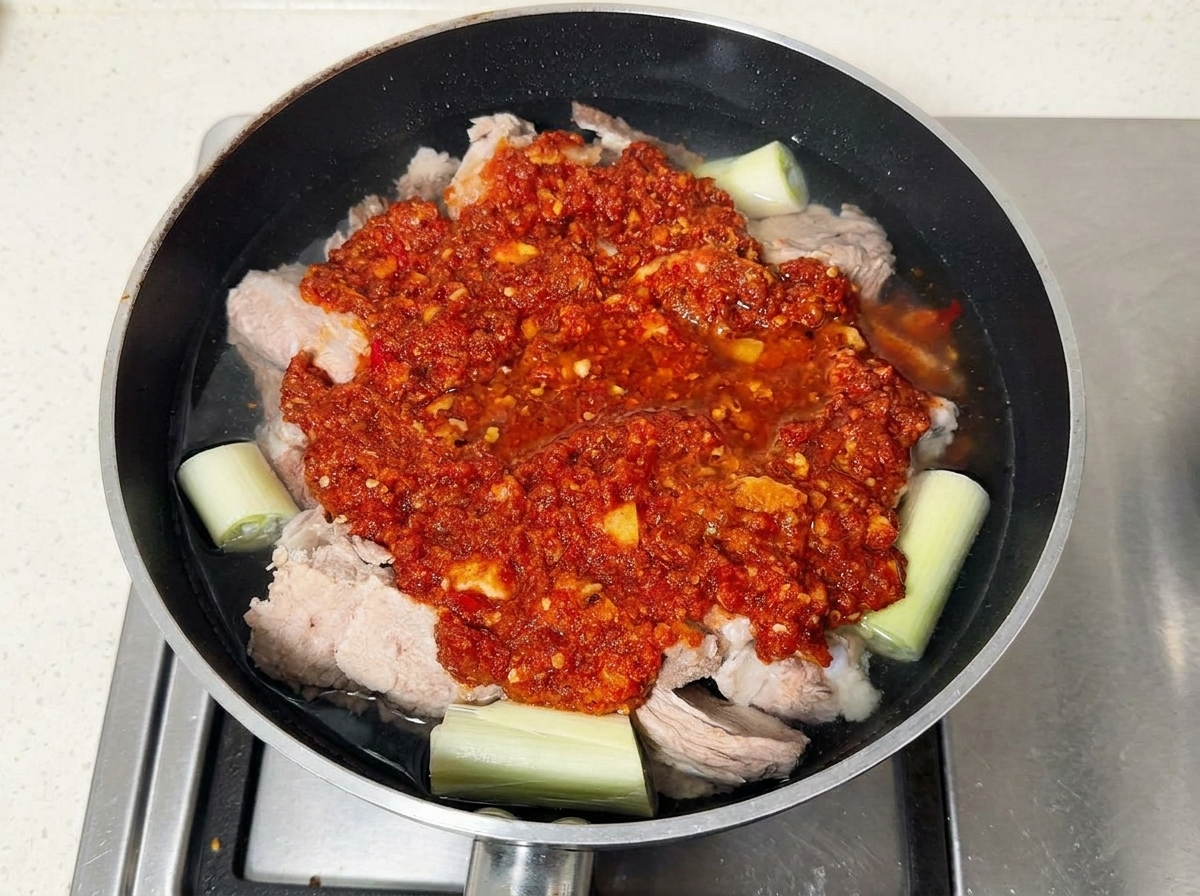 Travers de porc recouverts de pâte de piment rouge baignant dans leau dans une sauteuse.