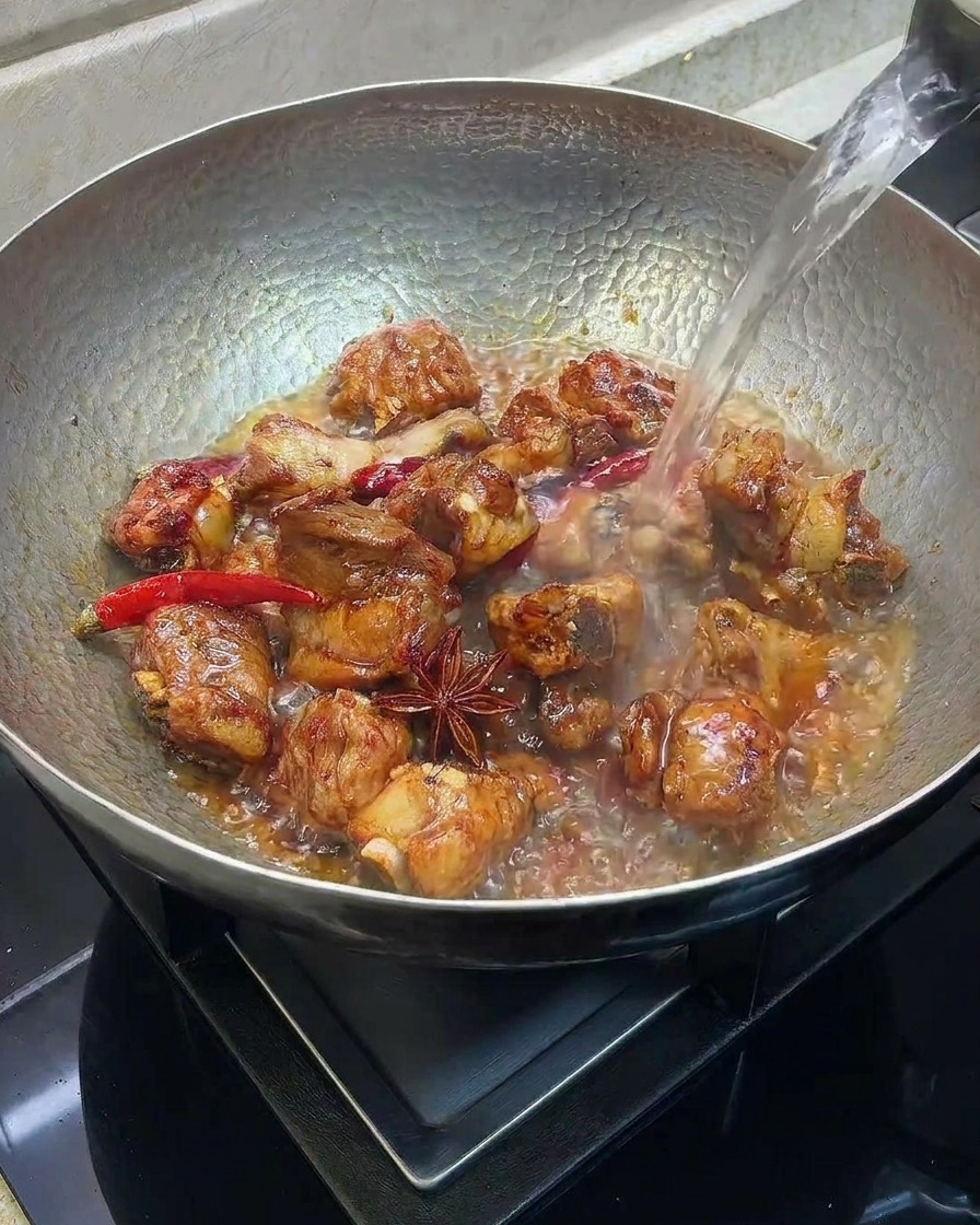 Eau chaude versée dans un wok contenant des travers de porc saisis et des épices.