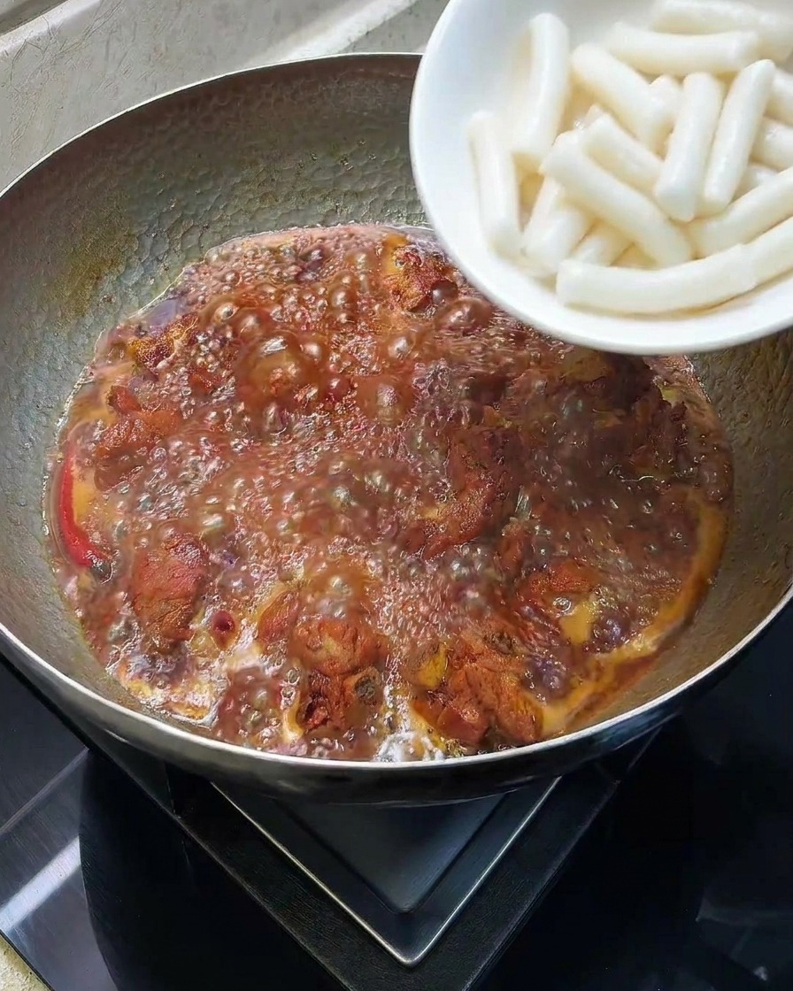 Gâteaux de riz blancs cylindriques ajoutés dans une marmite avec les travers de porc mijotés.