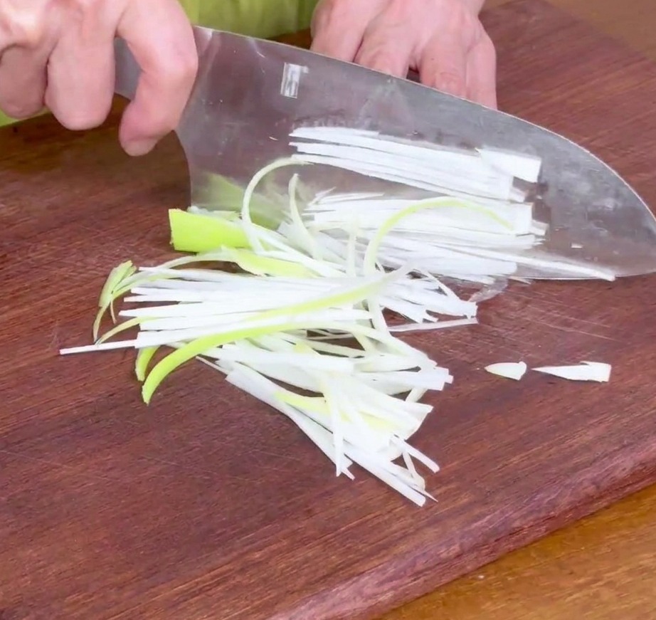 Lamelles doignons verts finement tranchées sur une planche à découper en bois, prêtes pour la marinade.