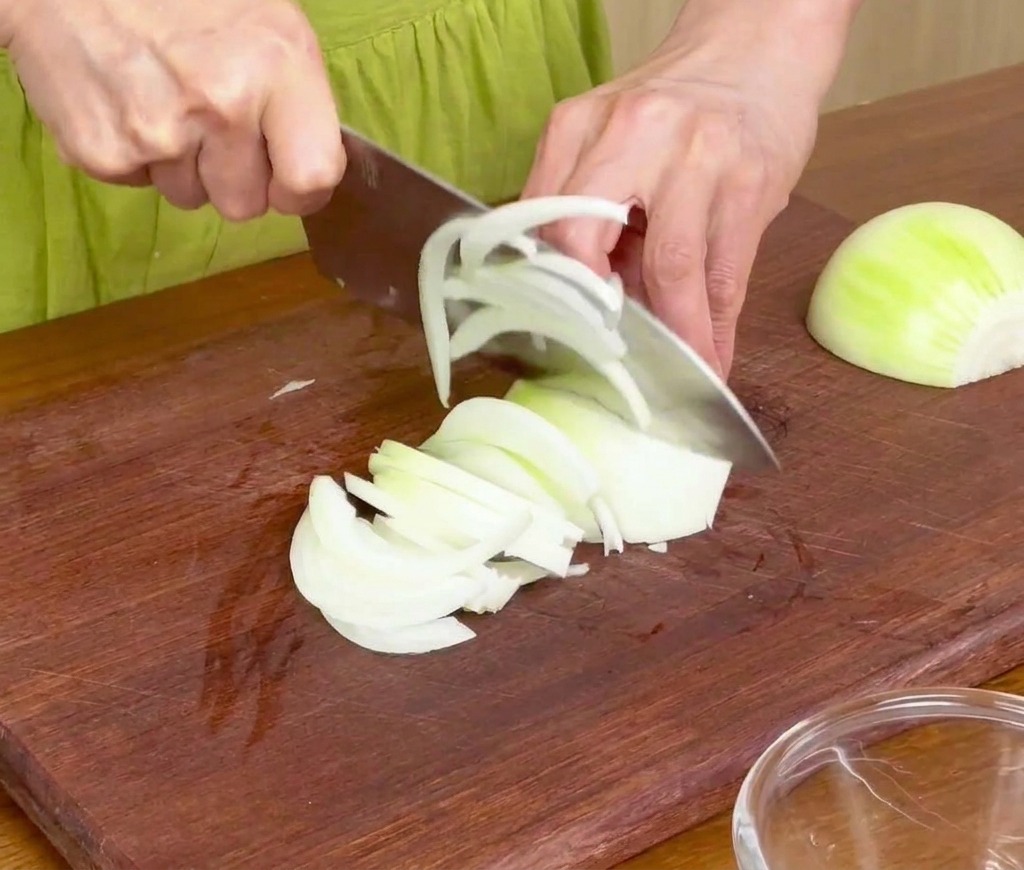 Oignon blanc tranché en fines lamelles sur une planche à découper en bois avec un couteau de chef.