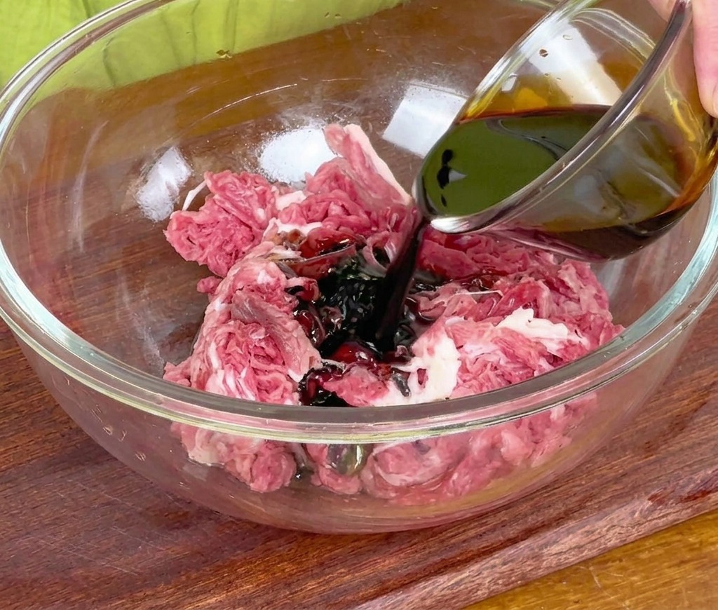 Verser de la sauce soja foncée dun petit bol en verre sur le bœuf cru dans un grand saladier en verre.