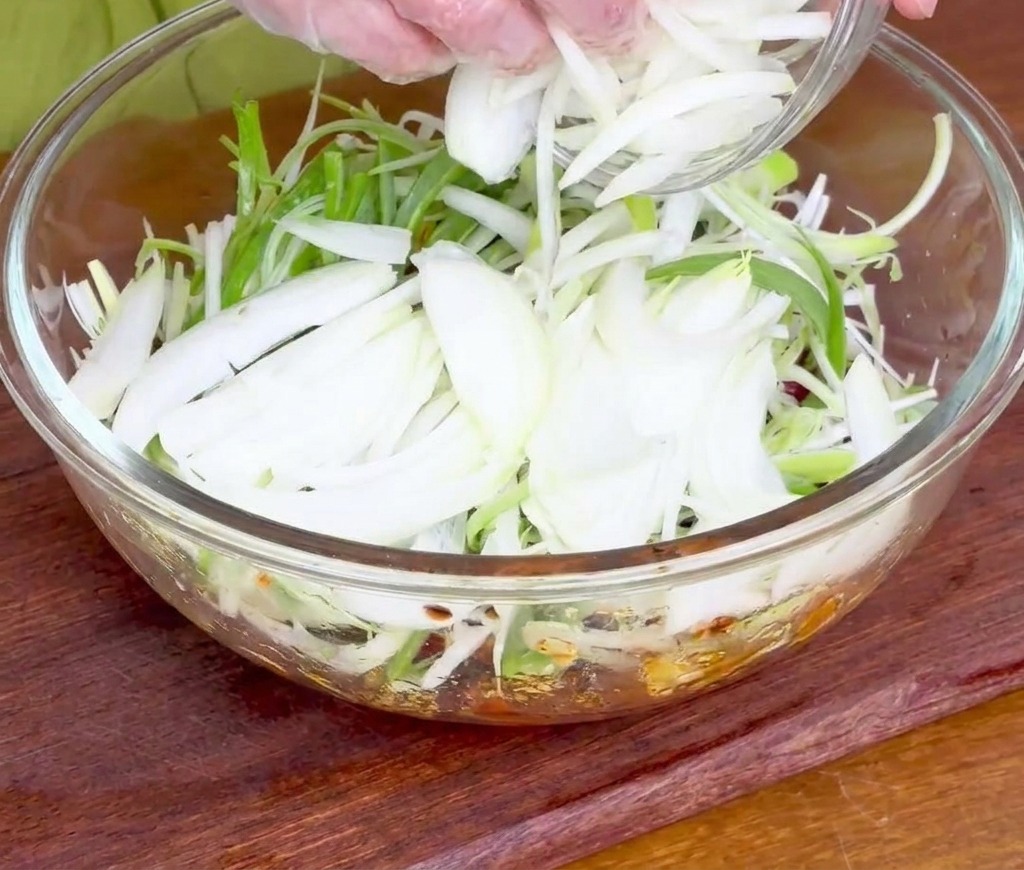 Mains ajoutant une poignée doignons blancs et verts tranchés sur le bœuf en marinade.