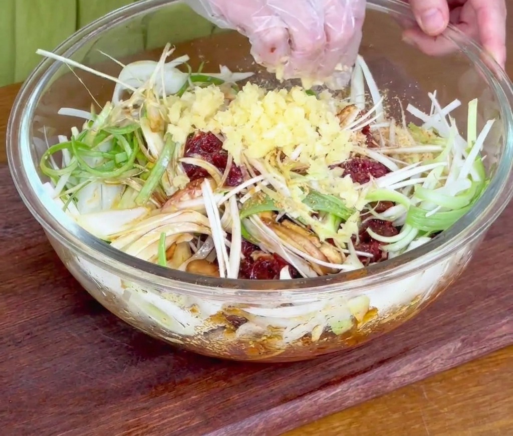 Une main saupoudrant de lail fraîchement haché sur le bœuf et les oignons dans un bol en verre.