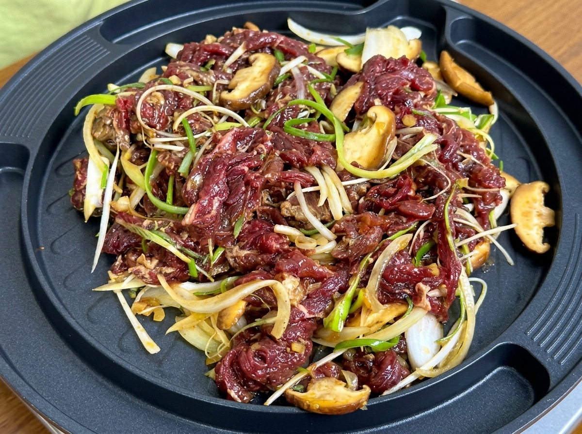 Bœuf mariné avec des tranches doignon et de champignon grésillant sur une poêle à griller circulaire.