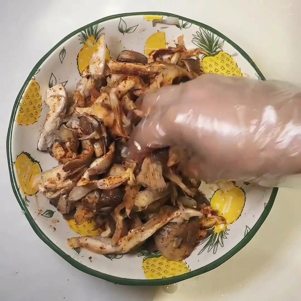 Main gantée mélangeant les champignons assaisonnés dans un bol.