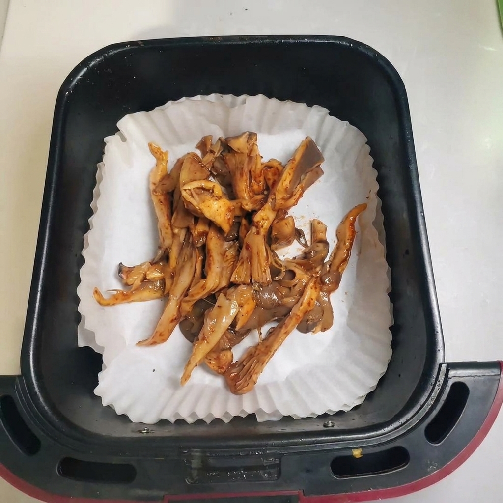 Champignons répartis dans un panier de friteuse à air sur du papier cuisson.