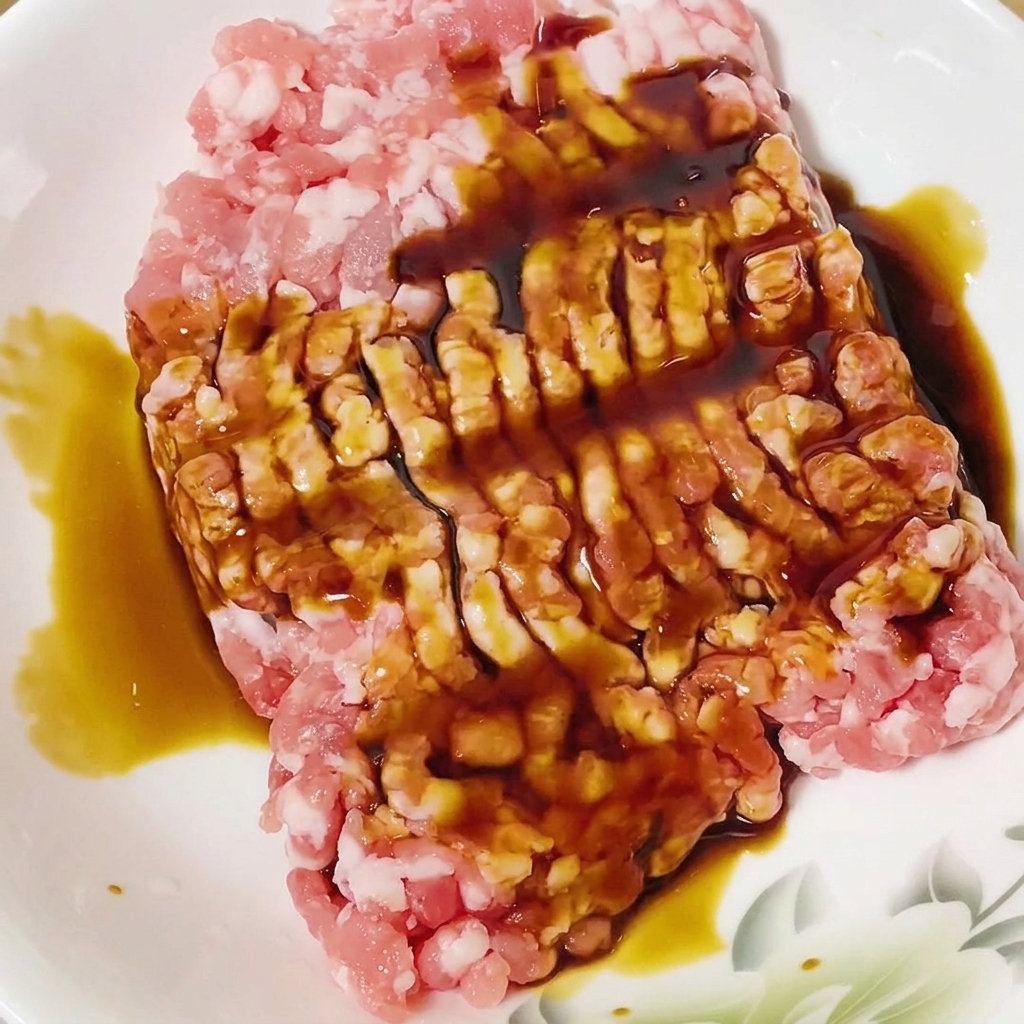 Sauce soja versée sur du porc haché cru dans un bol blanc.