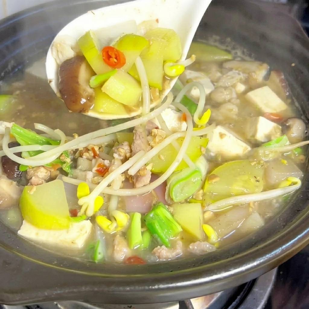 Une cuillère en métal mélangeant une grosse portion de pâte de soja fermentée dans le bouillon de ragoût bouillonnant.