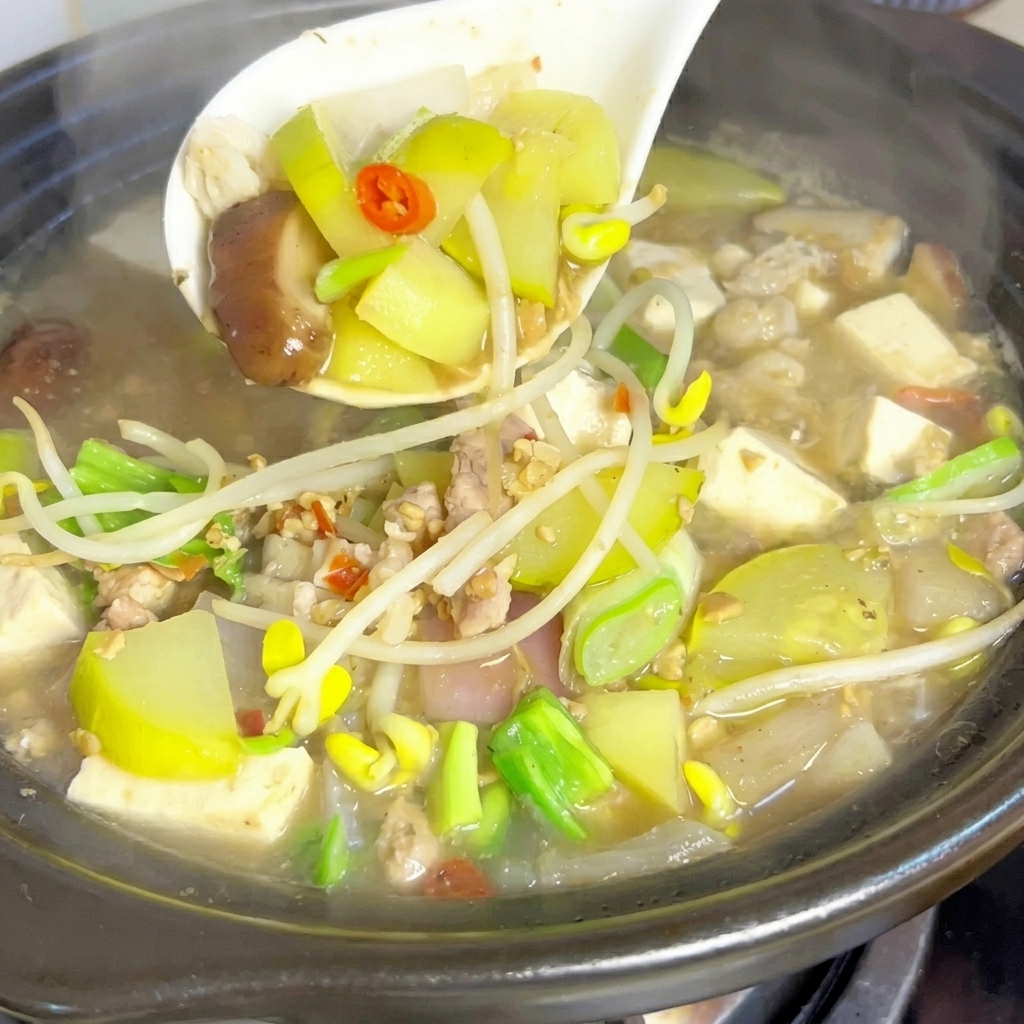 Une louche blanche soulevant délicatement un mélange de légumes, de tofu et de viande dune marmite en terre cuite fumante et bouillonnante de ragoût à la pâte de soja.