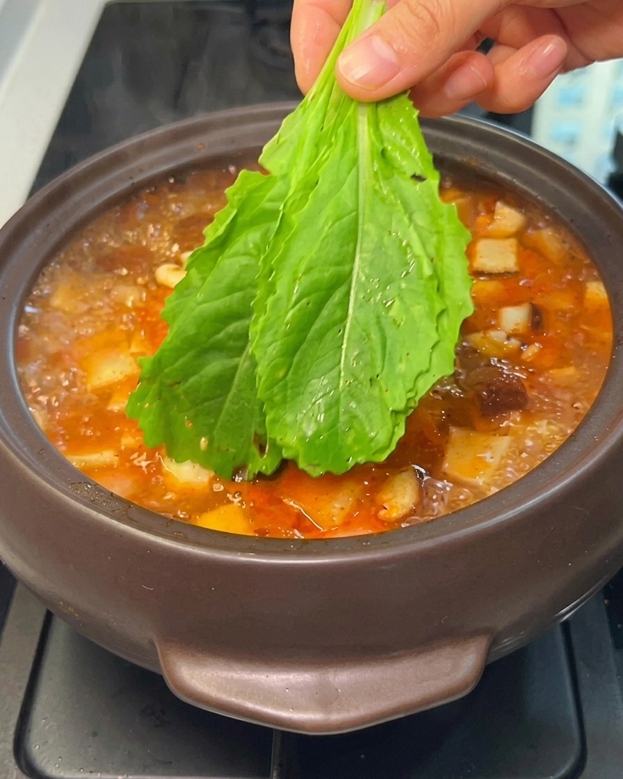 Main déposant des légumes verts frais dans le ragoût coréen bouillant.