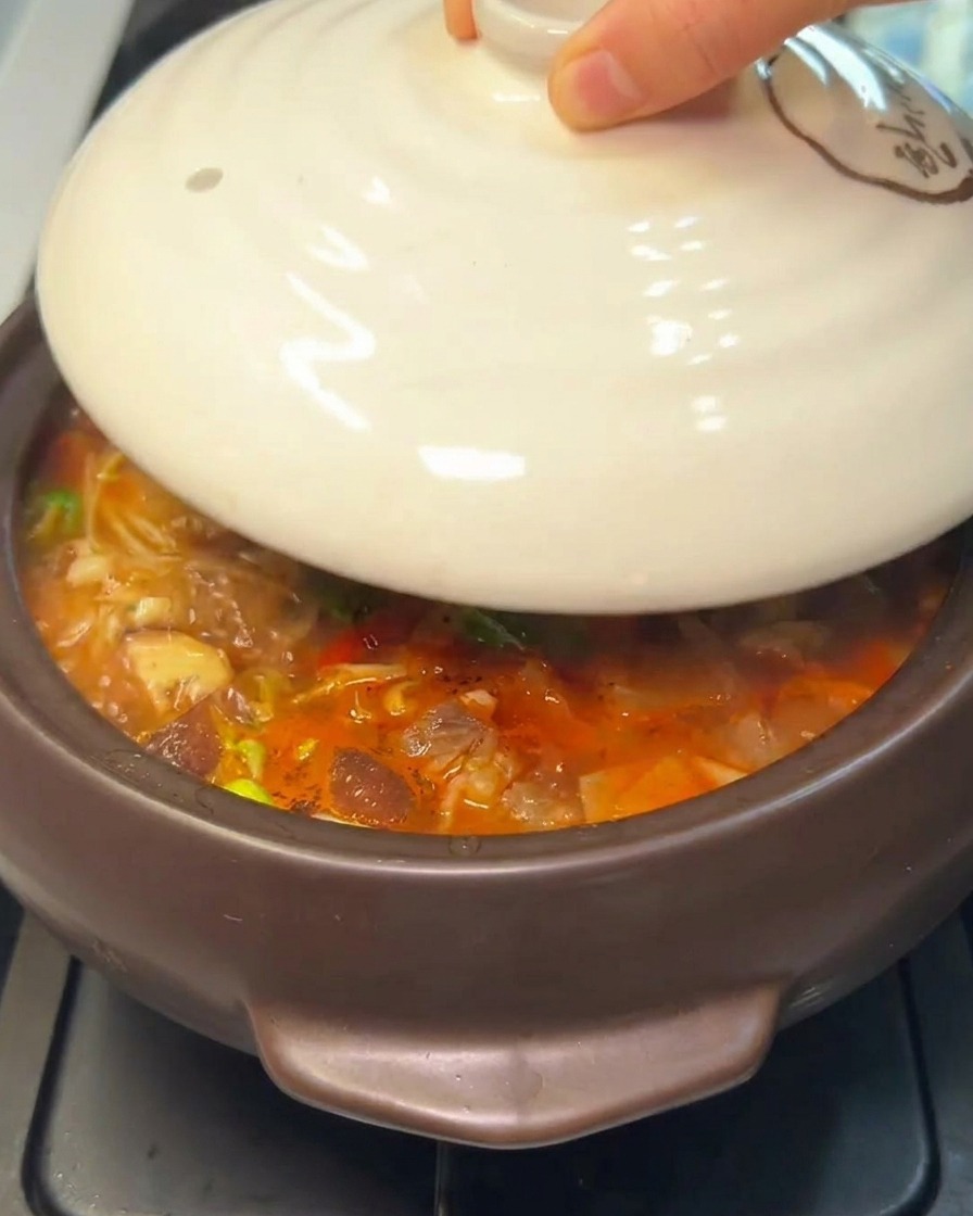 Main posant un couvercle en céramique sur un pot en pierre fumant.