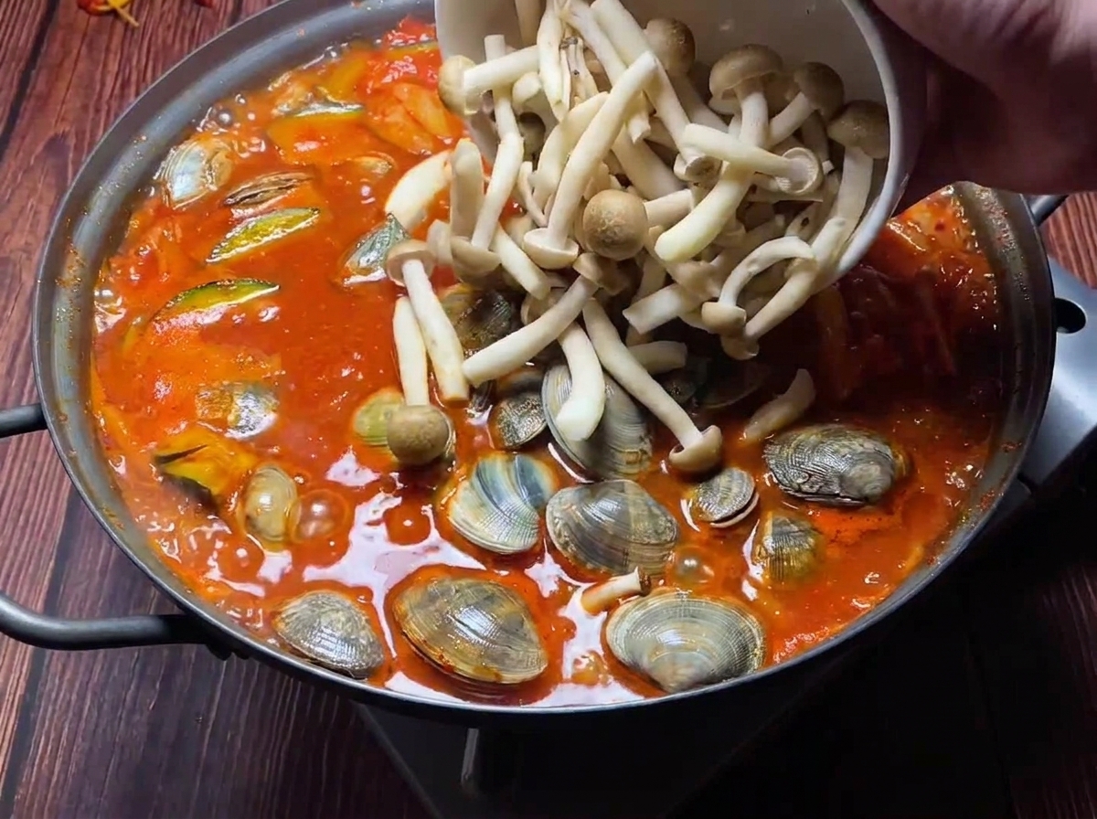Des palourdes fraîches et des champignons assortis ajoutés dans un ragoût rouge bouillonnant.