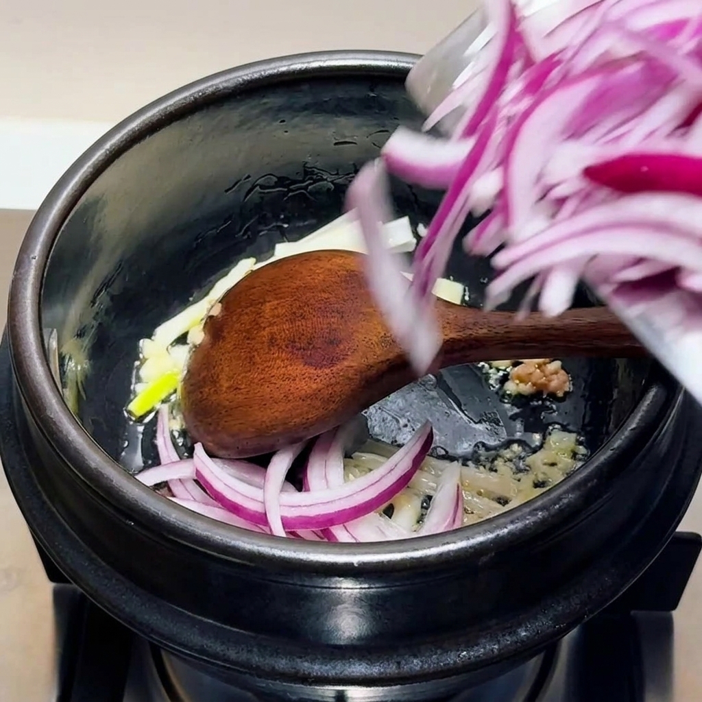 Oignons rouges émincés, ail haché et blancs doignons verts remués dans un pot noir avec une cuillère en bois.