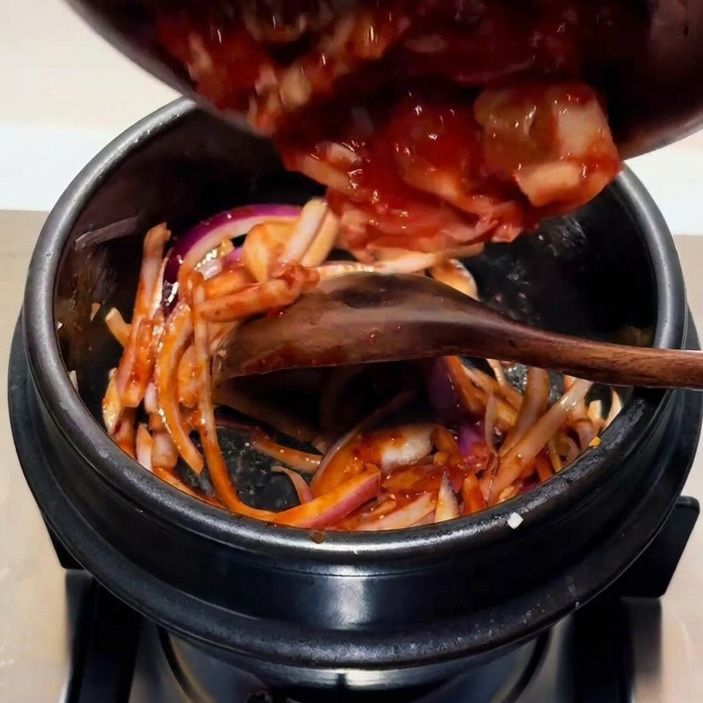 Kimchi haché ajouté dans le pot avec la base doignons sautés et de sauce.