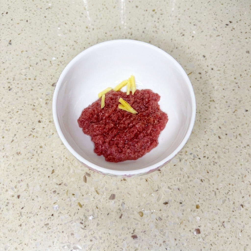 Bœuf haché dans un bol blanc mélangé avec de la sauce soja, de lhuile et de la fécule, agrémenté de tranches de gingembre.